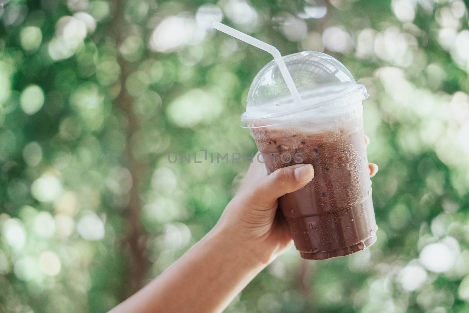 Woman hand holding glass of ice chocolate on wood table, selective focus