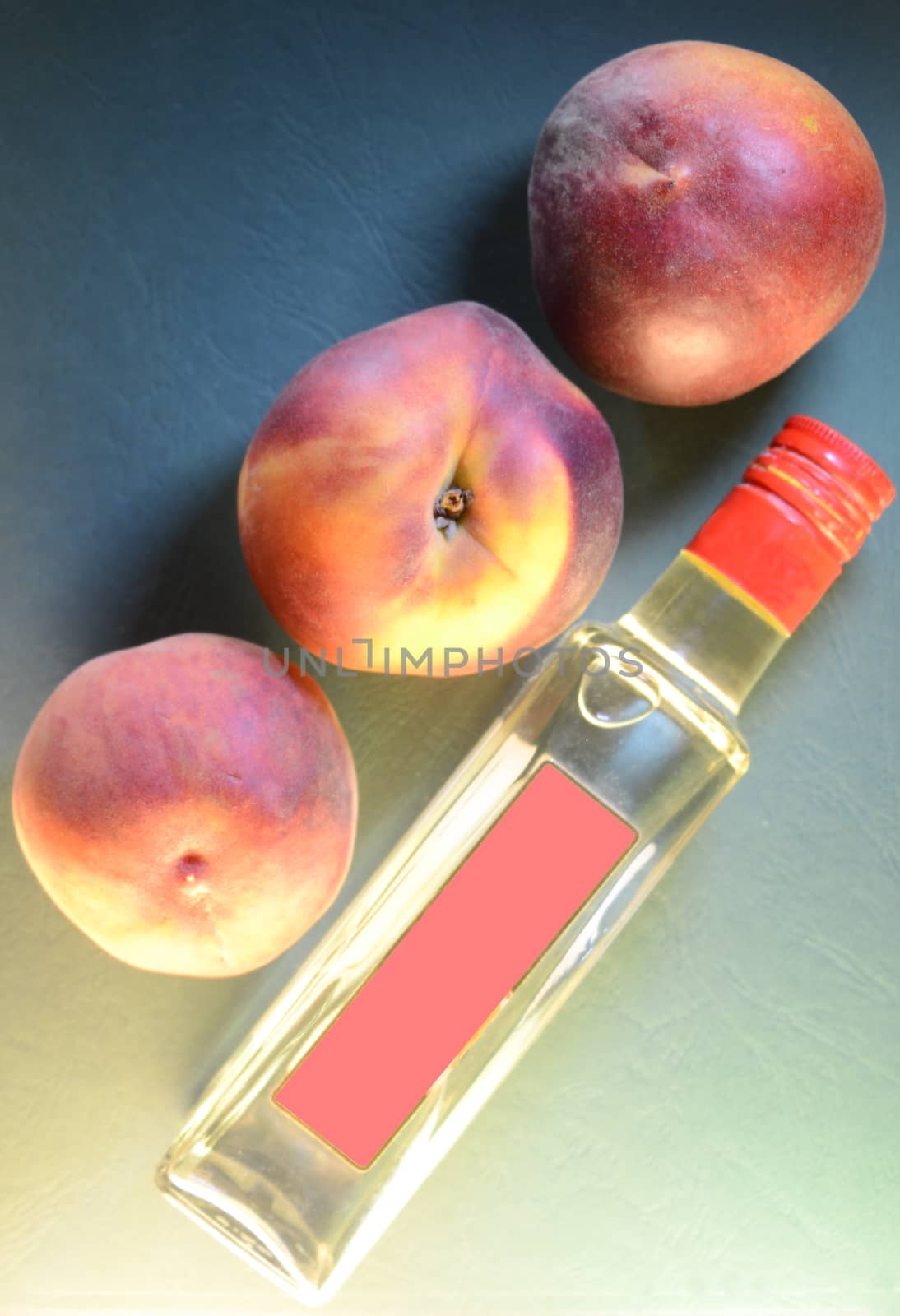 three ripe peaches close-up over a bottle with a pink label on an embossed leathery azure green background, top view