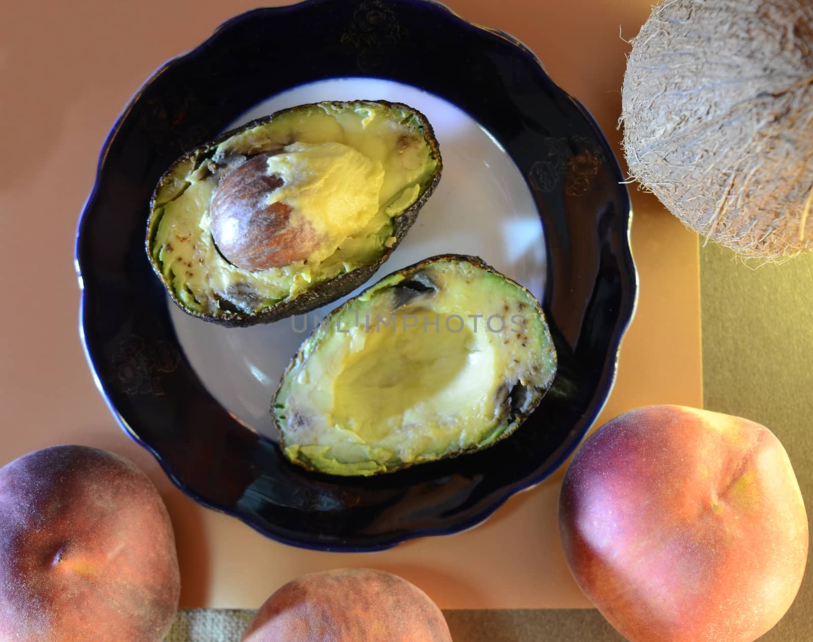 for dessert, two halves of a ripe avocado on a plate, and outside: three peaches and a coconut