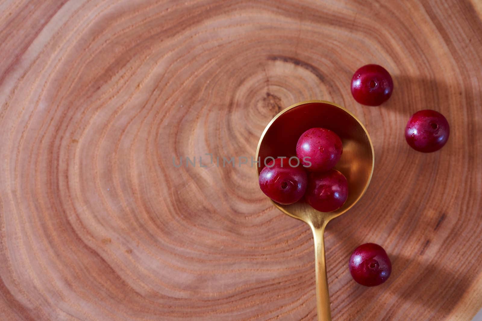 Ripe cherry berry on a wooden slice of wood in golden spoon. With copy space. by Xelar