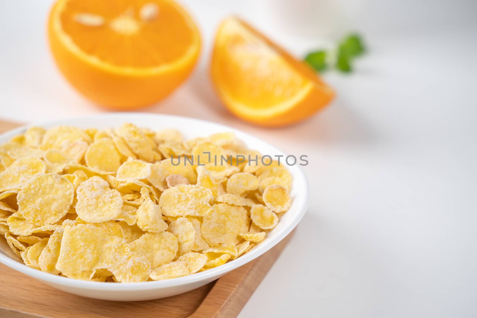 Corn flakes bowl sweeties with milk and orange on white background, close up, fresh and healthy breakfast design concept.