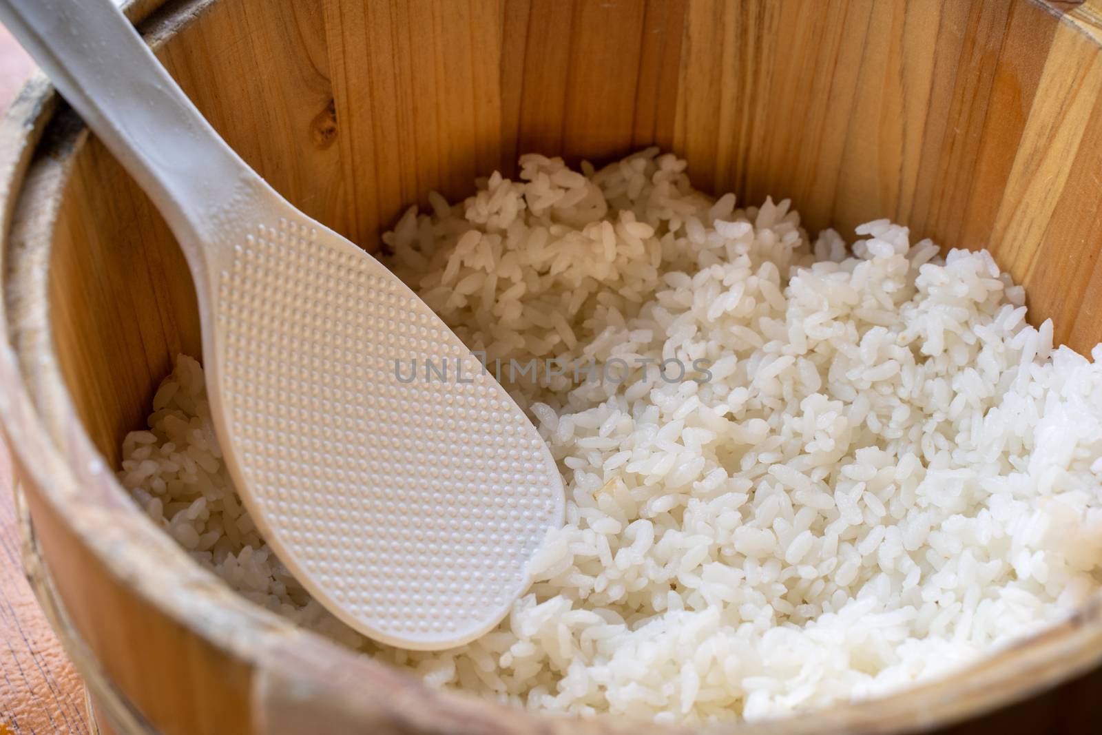 Delicious cooked plain rice in a big wooden bowl ready-to-eat with white rice spatula spoon at restaurant table, close up, lifestyle.