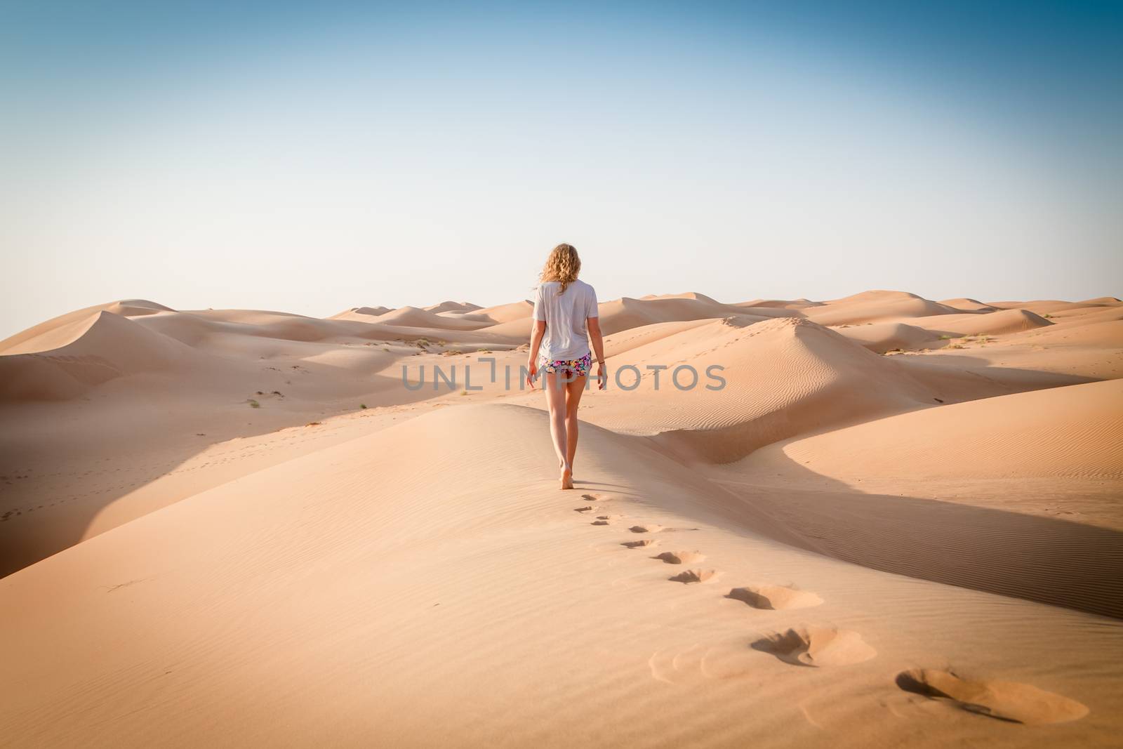 Blonde female Caucasian traveler leaving footprints in sand dunes when walking in dessert in Oman.