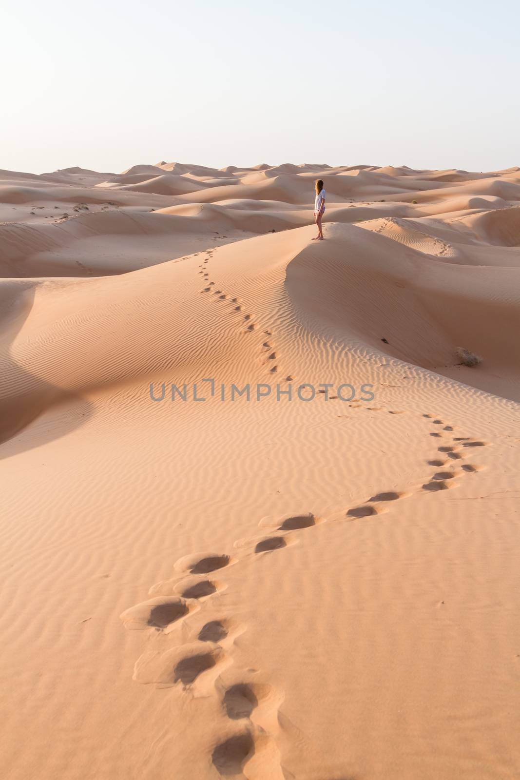 Blonde female Caucasian traveler leaving footprints in sand dunes when walking in dessert in Oman by kasto