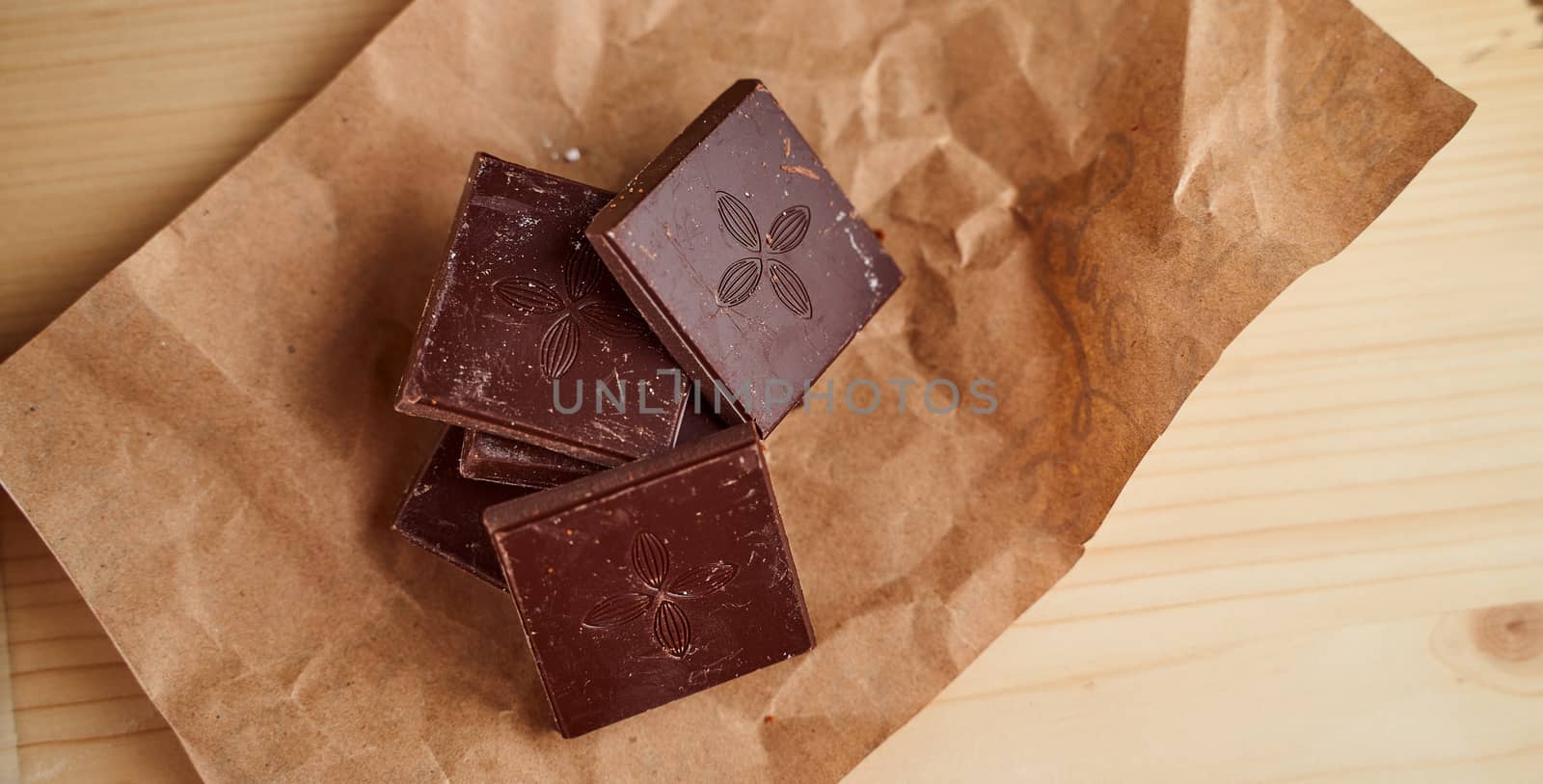Pieces of chocolate bar lie on crafted brown paper. High quality photo