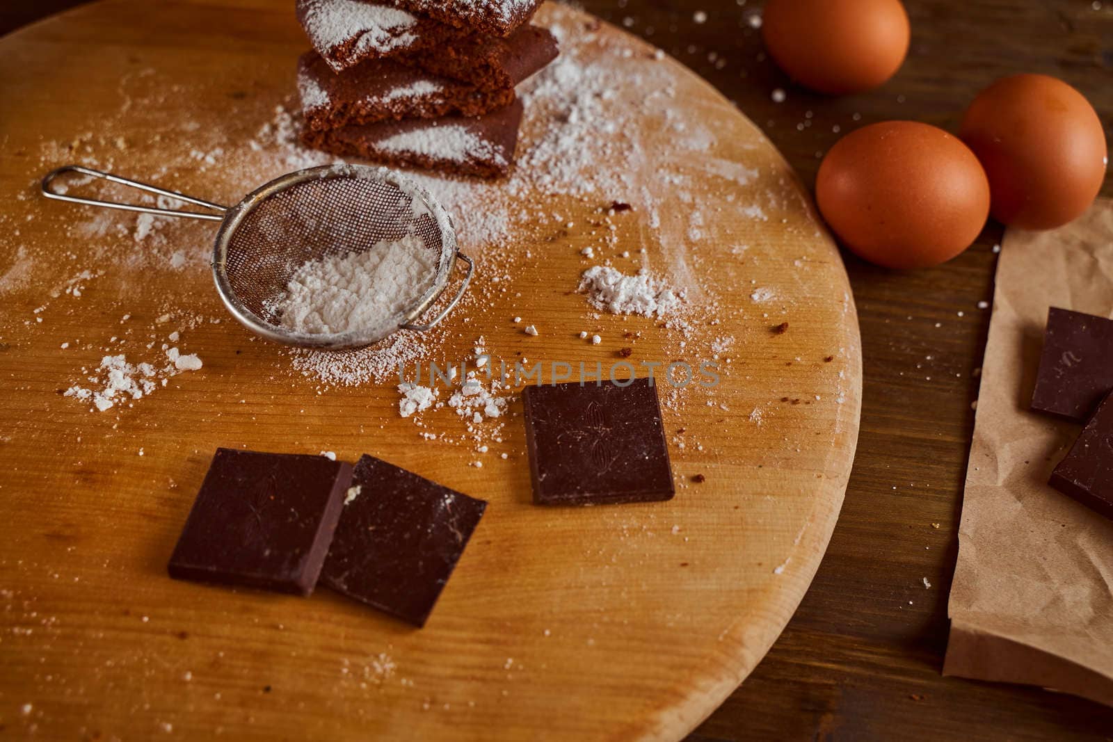 Composition of Chocolate cakes stacked on a wooden table. next to it are eggs and pieces of chocolate. blurred background. High quality photo
