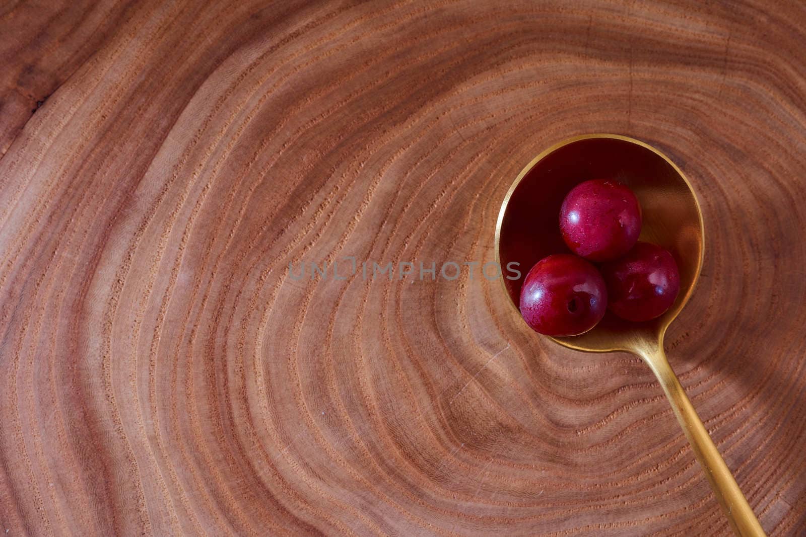 Ripe cherry berry on a wooden slice of wood in golden spoon. High quality photo