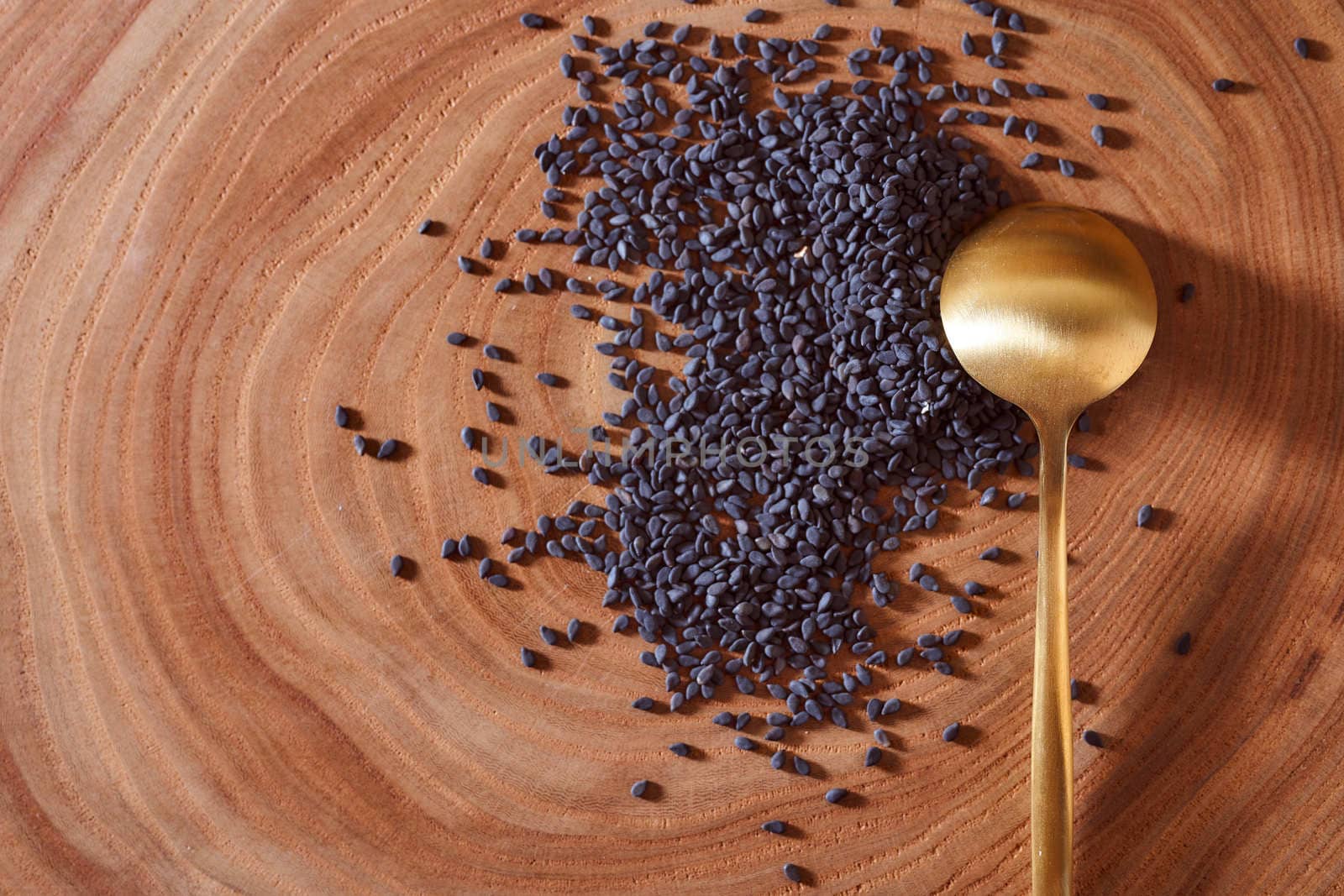 Black sesame with golden spoon lies on a wooden slice. Close-up. Macro effect photo. With copy space. High quality photo