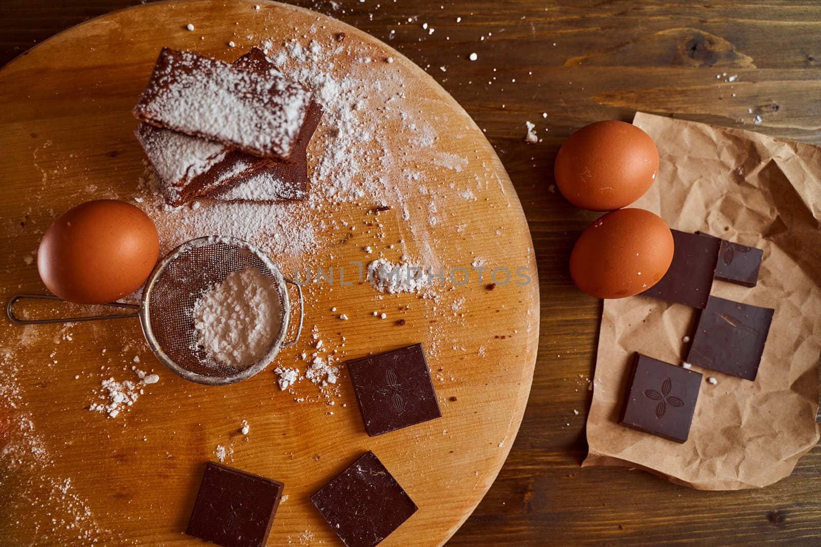 Composition of Chocolate cakes stacked on a wooden table. next to it are eggs and pieces of chocolate. Top view. High quality photo