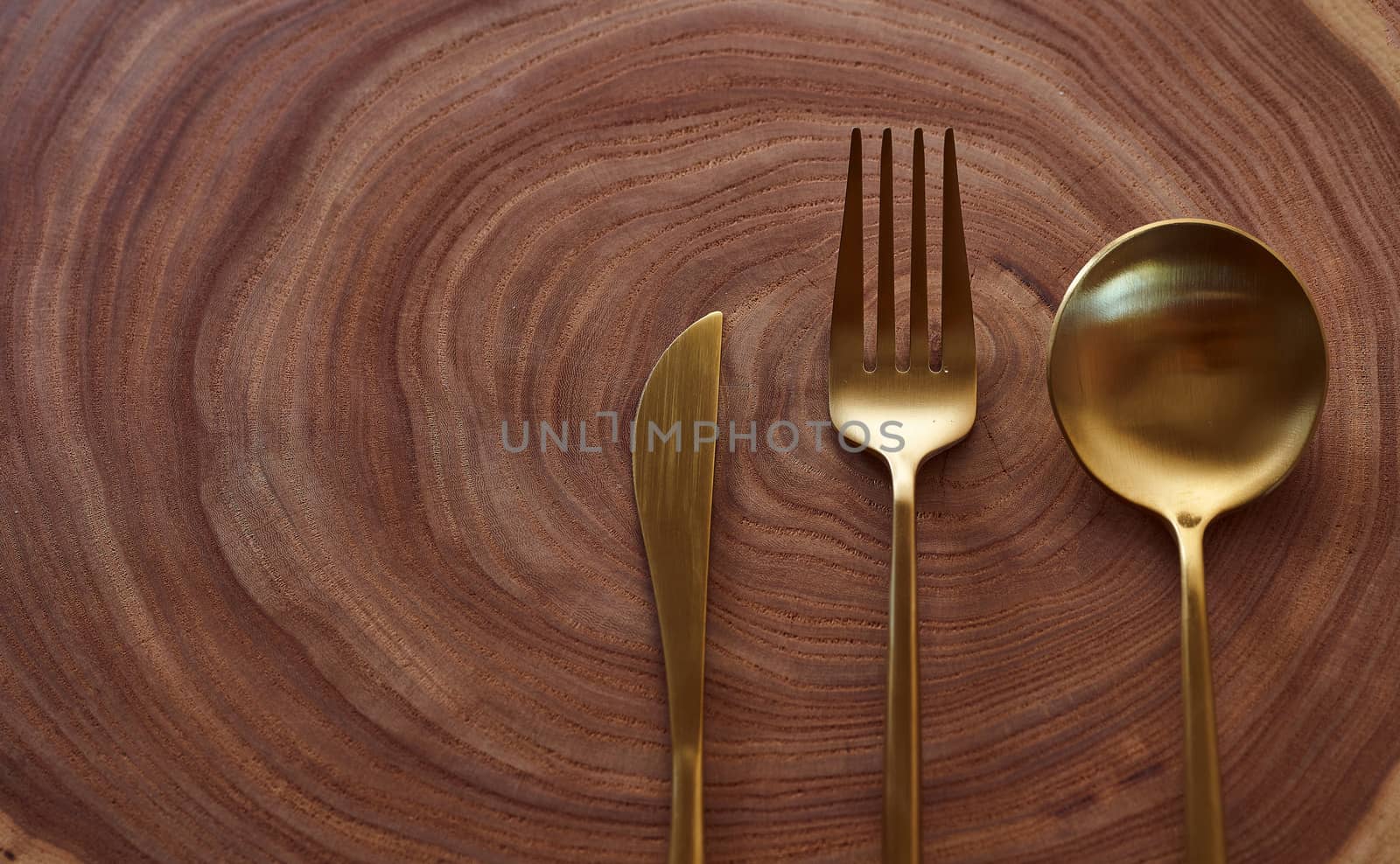 The golden knife, fork and spoon lies on a slice of a tree. wooden table. With copy space. High quality photo