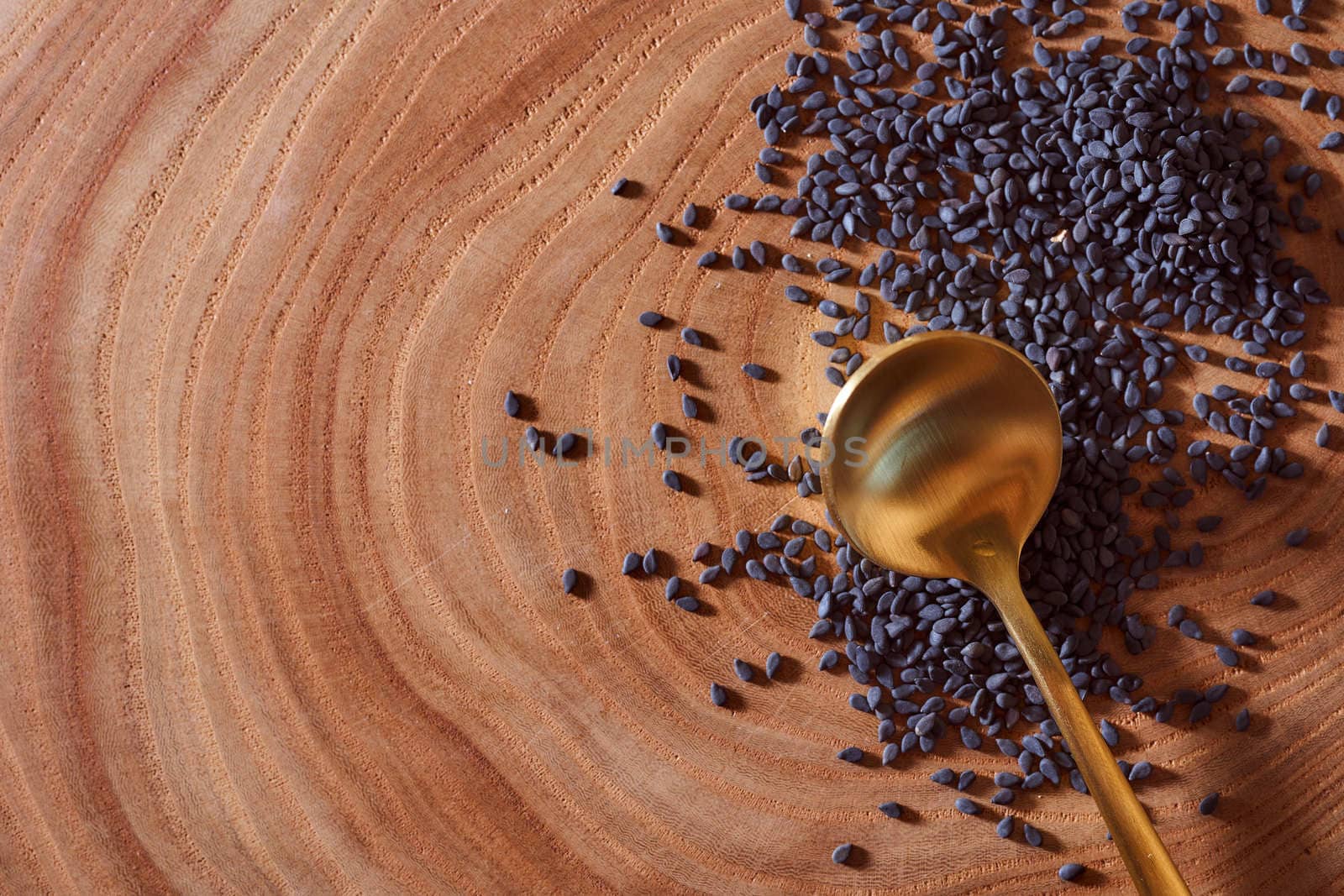 Black sesame with golden spoon lies on a wooden slice. Close-up. Macro effect photo. With copy space. High quality photo