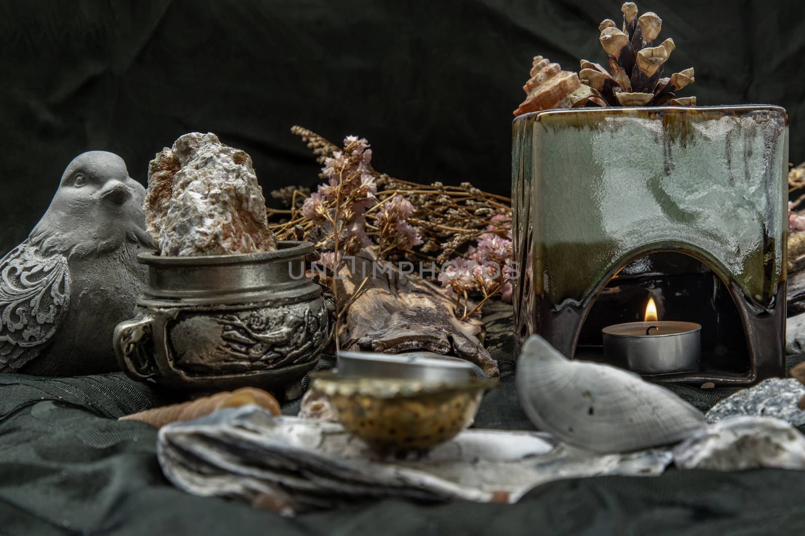 Beauty composition with Burning candle aroma oil lamp and Dry flower petals and Pine cones, Natural pine wood disc, Stones and Shells, Himalayan salt on dark background. Aromatherapy concept.
