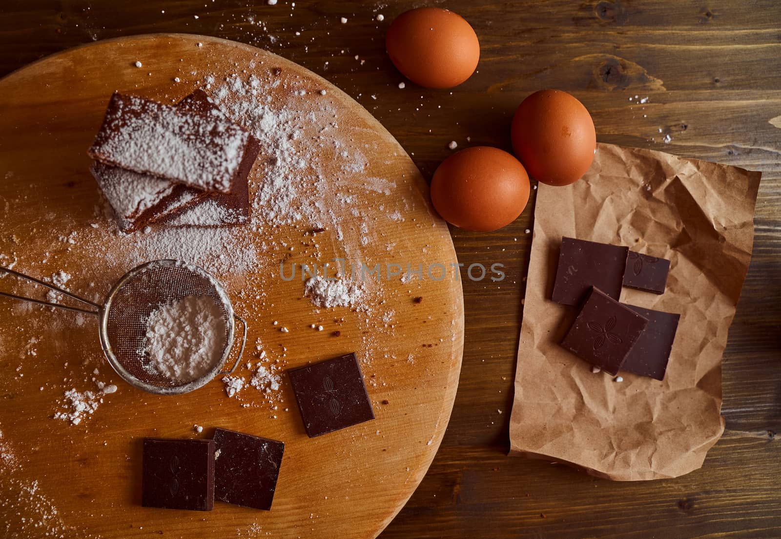 Composition of Chocolate cakes stacked on a wooden table. next to it are eggs and pieces of chocolate. Top view. High quality photo