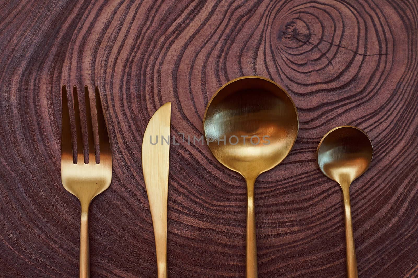 Composition concept.The golden fork, knife, and spoons lies on a slice of a tree. wooden table. With copy space. High quality photo