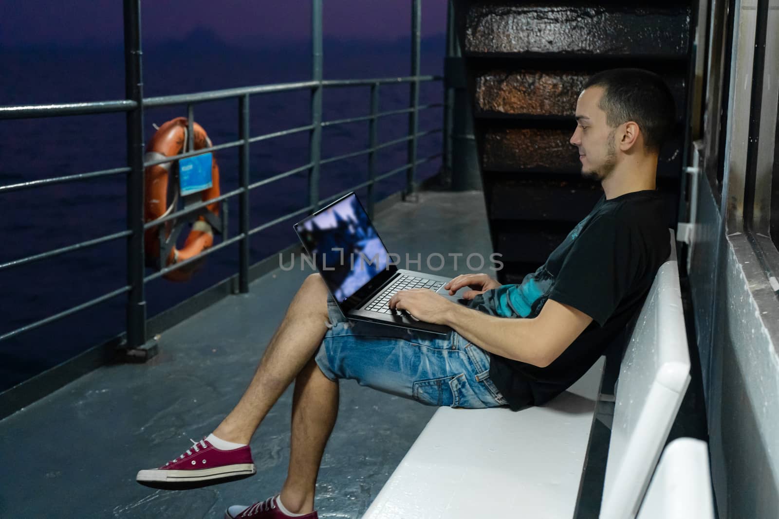 A young man works on a laptop on the deck of a ship. Remote work by Try_my_best