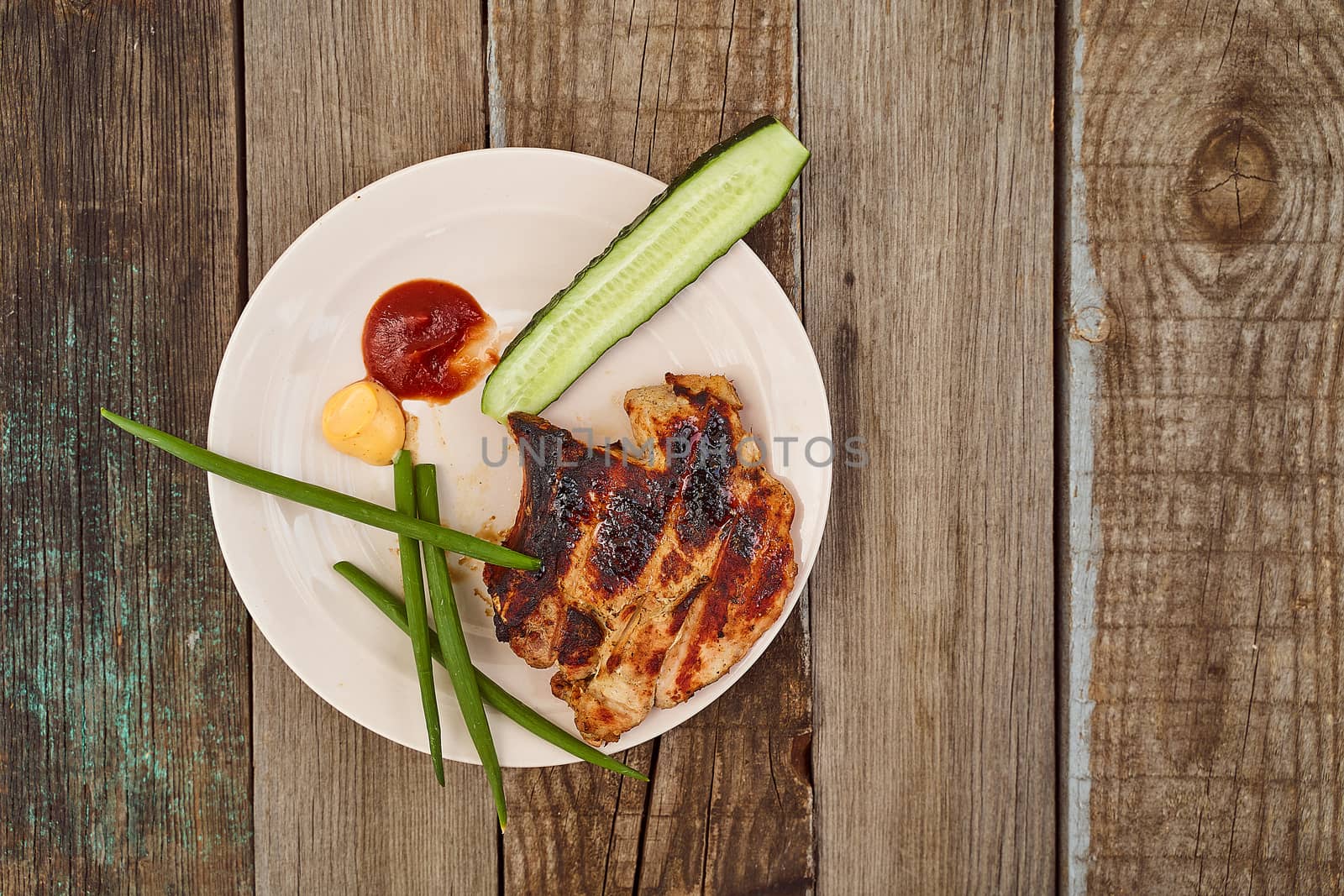 Ready pork steak in a white plate with green onions on an old wooden table. High quality photo