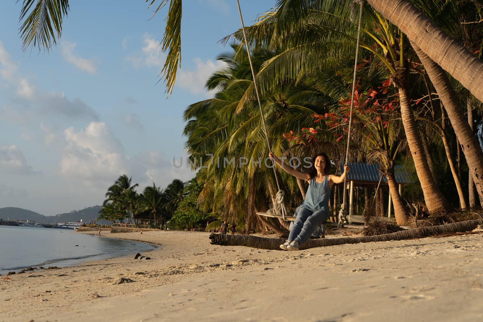The girl on the beach rides on a swing during sunset. Sunset in the tropics, enjoying nature. Swing tied to a palm tree by the ocean.