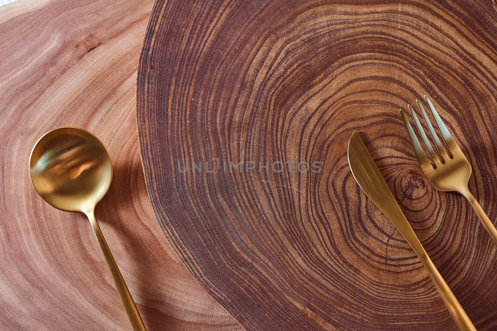 The golden spoon, knife and fork lies on a slice of a tree. wooden table. With copy space. High quality photo