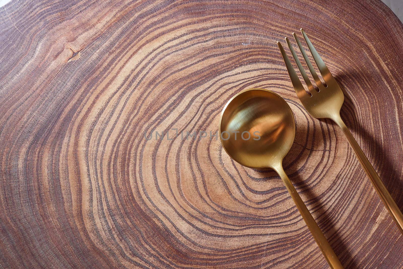 The golden fork and spoon lies on a slice of a tree. wooden table. With copy space. High quality photo