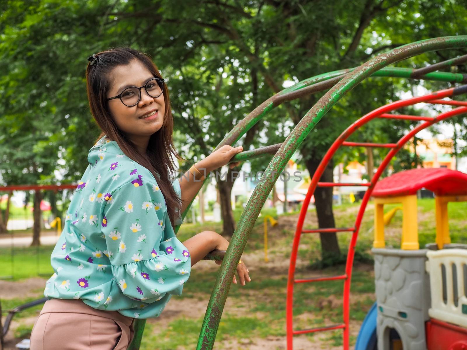 Portrait of Asian women wearing eyes Stand on an iron ladder in the park Wearing a green striped shirt Light purple pants And have a green tree background.