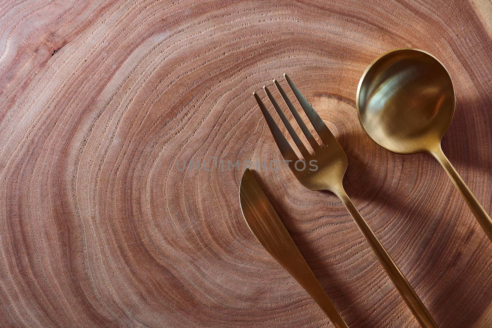 The golden knife, fork and spoon lies on a slice of a tree. wooden table. With copy space. High quality photo