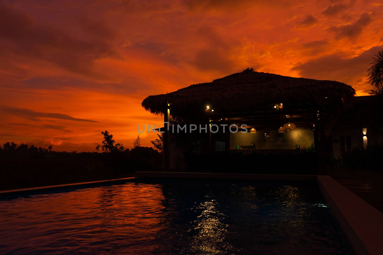 Beautiful orange fiery sunset in the tropics. Street canopy from hay, next to the pool and overlooking the rice field