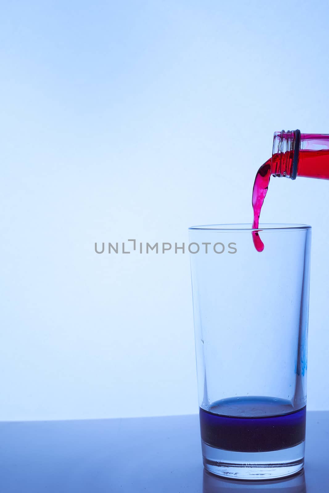 pour red wine into a glass cup with blue liquid. Hight quality photo