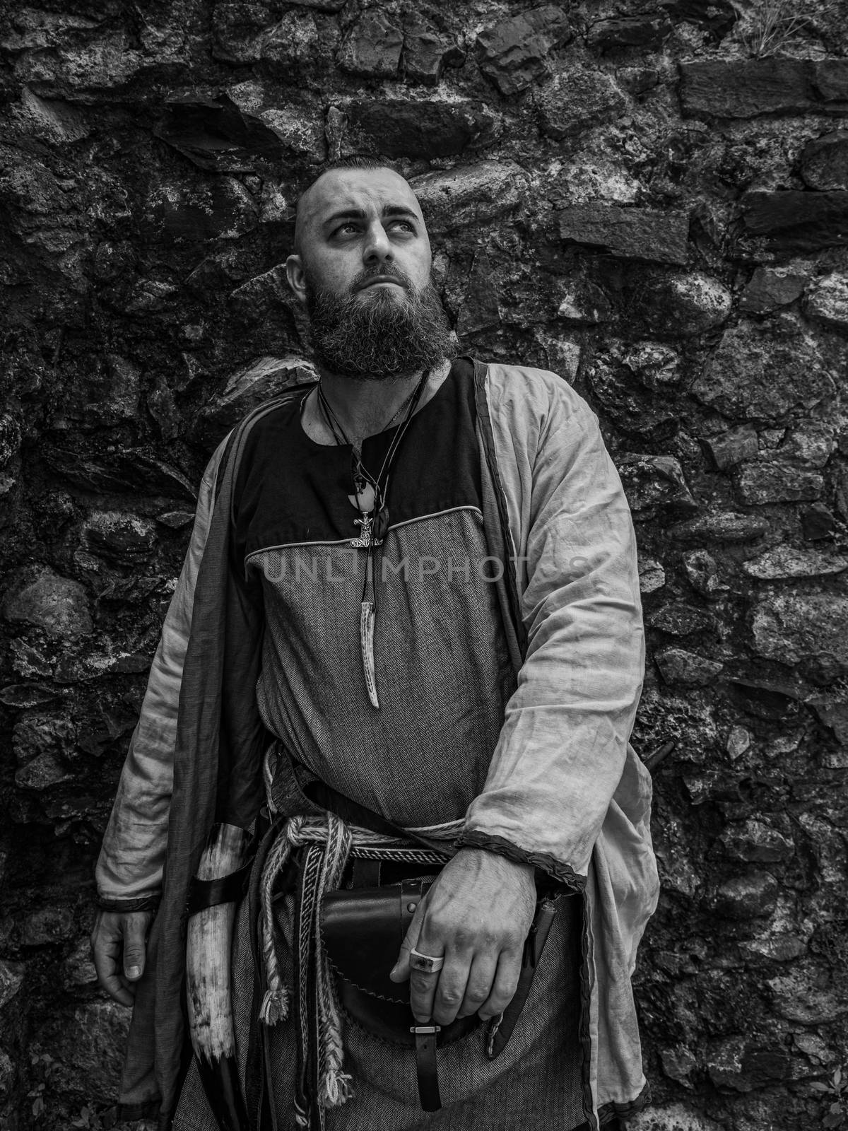 Viking warrior portrait with thick beard in front of a stone wall, black and white historical reenactment image