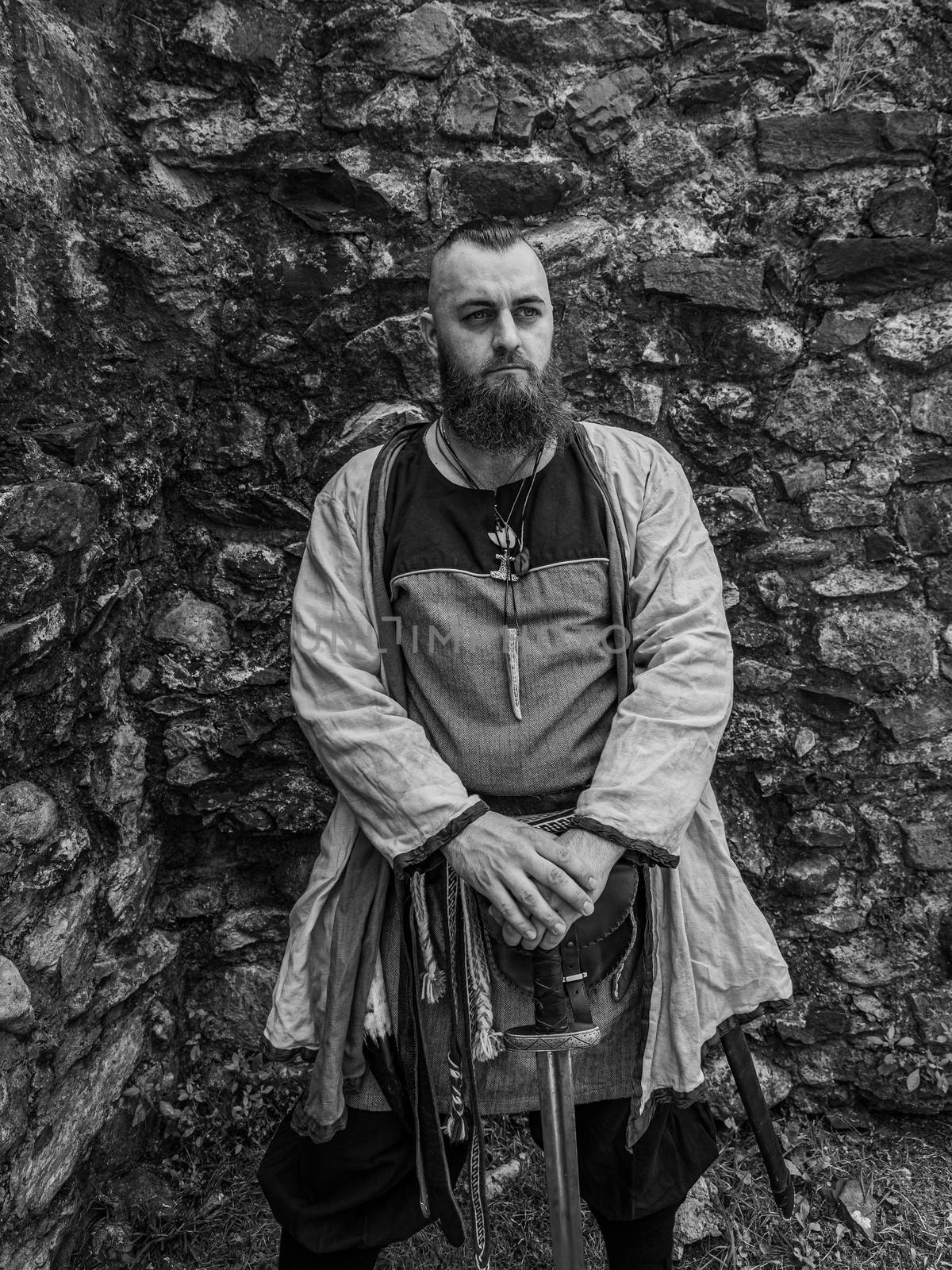 Viking warrior portrait with thick beard in front of a stone wall, black and white historical reenactment image