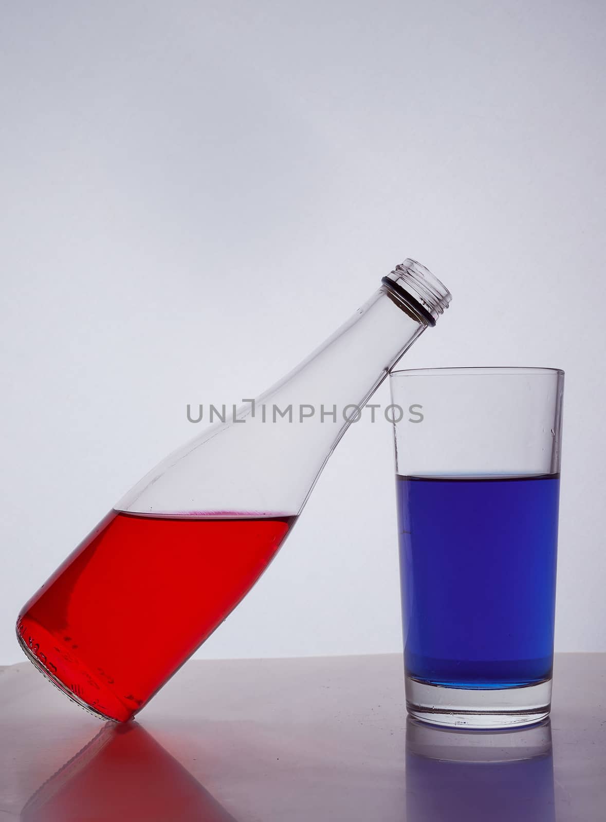 composition from a bottle and glasses with multicolored liquid on a white background. The bottle rests on a glass. Hight quality photo