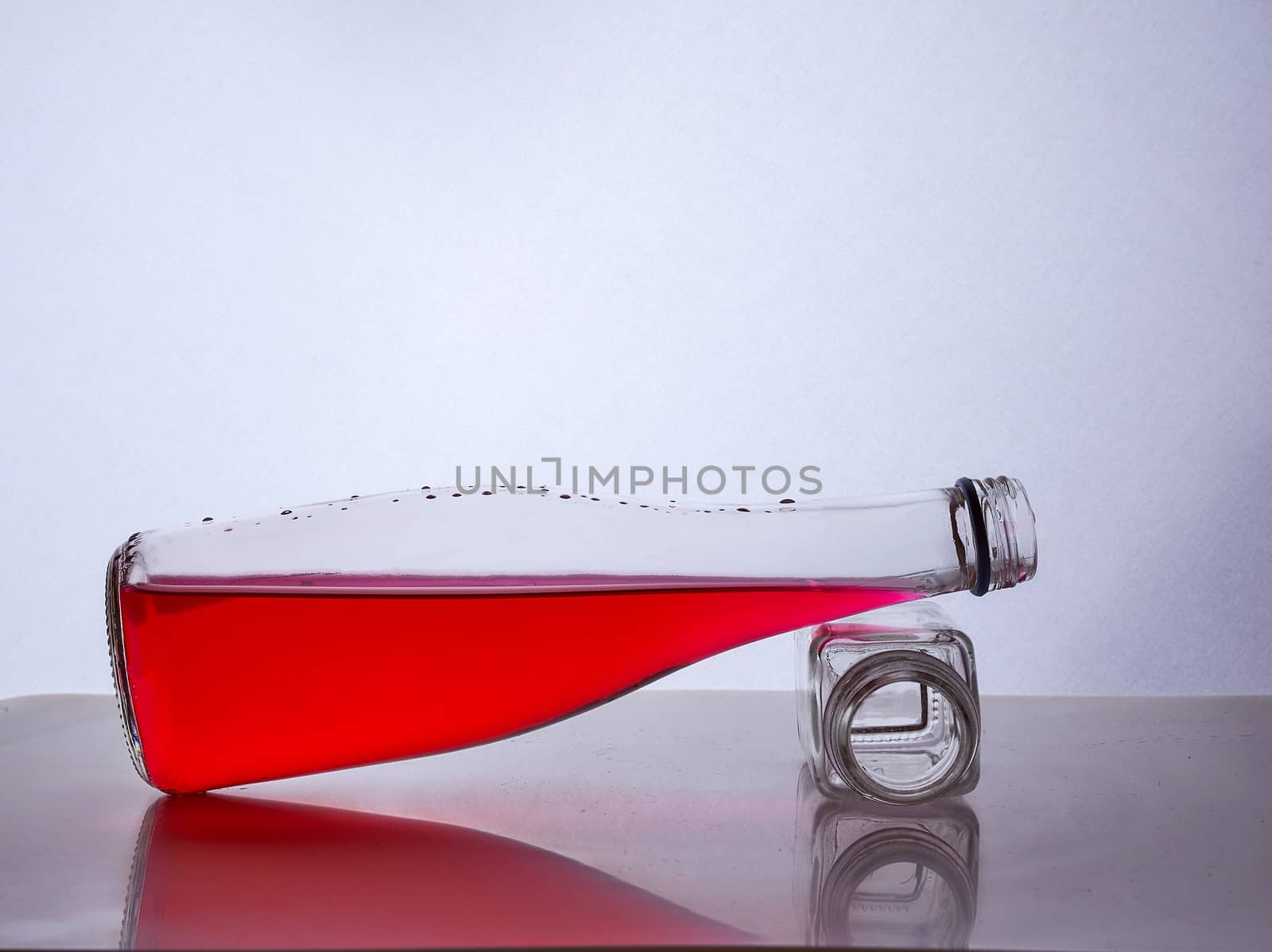 glass bottle with red liquid inside lies on a small bottle of white background. Hight quality photo