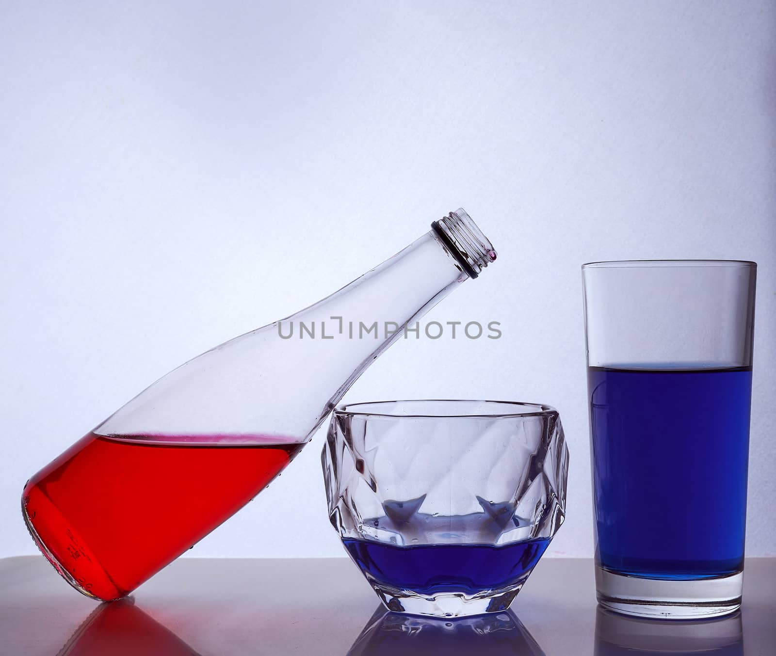 composition from a bottle and glasses with multicolored liquid on a white background. The bottle rests on a glass of whiskey. Hight quality photo