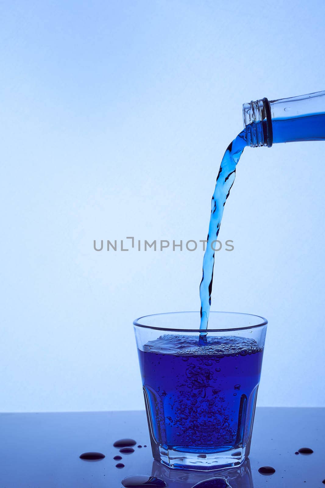 a blue liquid is poured into a glass of whiskey. Light blue background. Hight quality photo