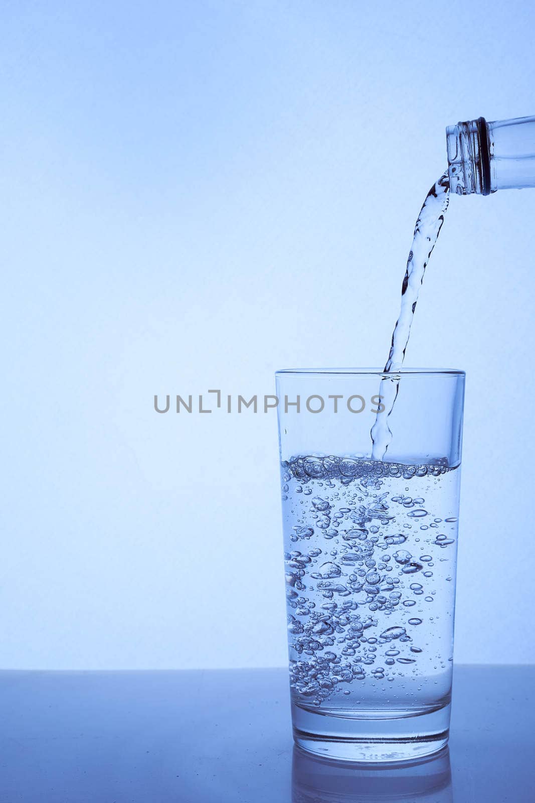 fresh clean water is poured from a bottle into a glass cup. Light background.. Hight quality photo