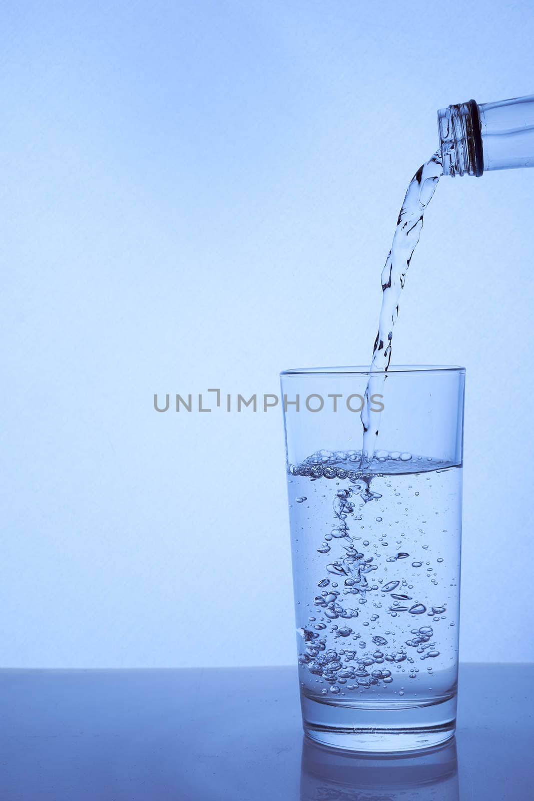 fresh clean water is poured from a bottle into a glass cup. Light background.. Hight quality photo