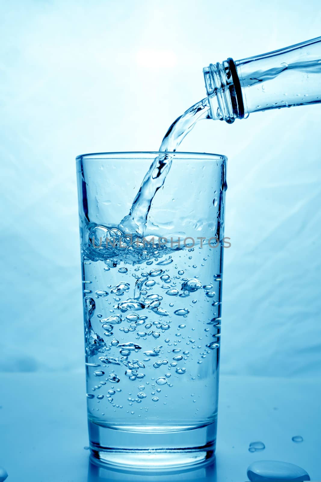 fresh clean water is poured from a bottle into a glass cup. Light background.. Hight quality photo