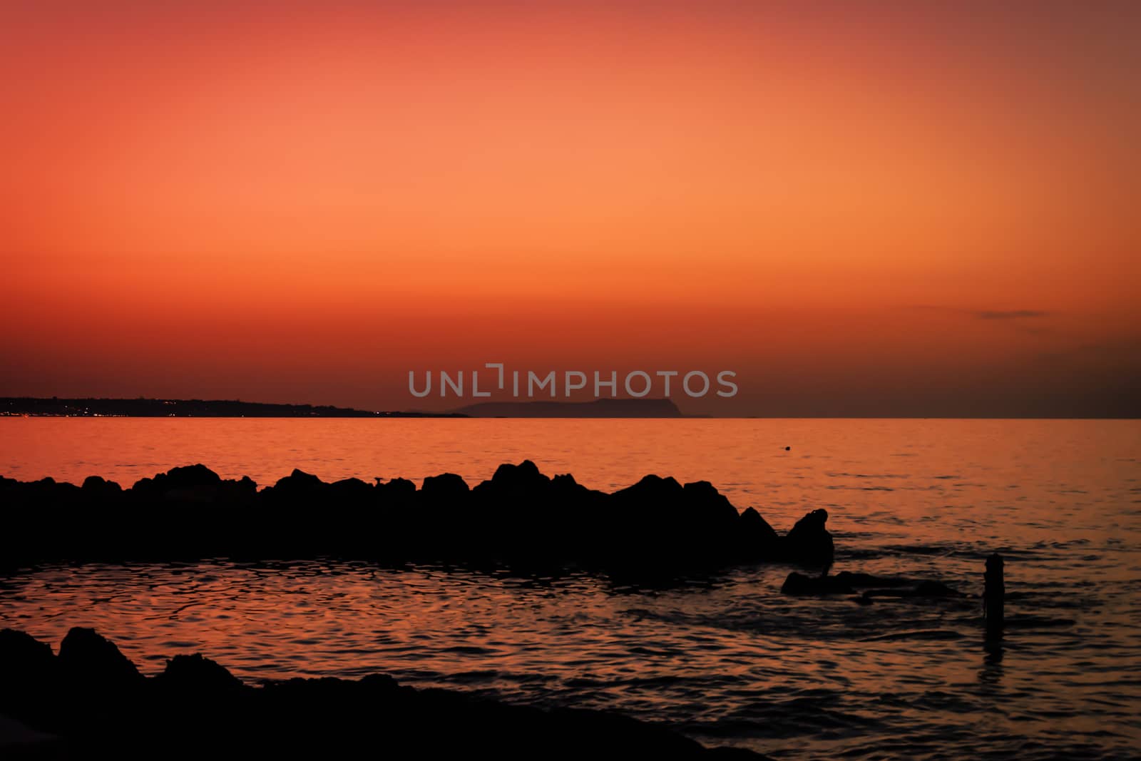 Skyline after sundown. Scenery of orange sky with rock silhouette and ocean waves. Orange sunset at shoreline photography. Waterfront tranquility in paradise on vacations. Majestic horizon wallpaper.