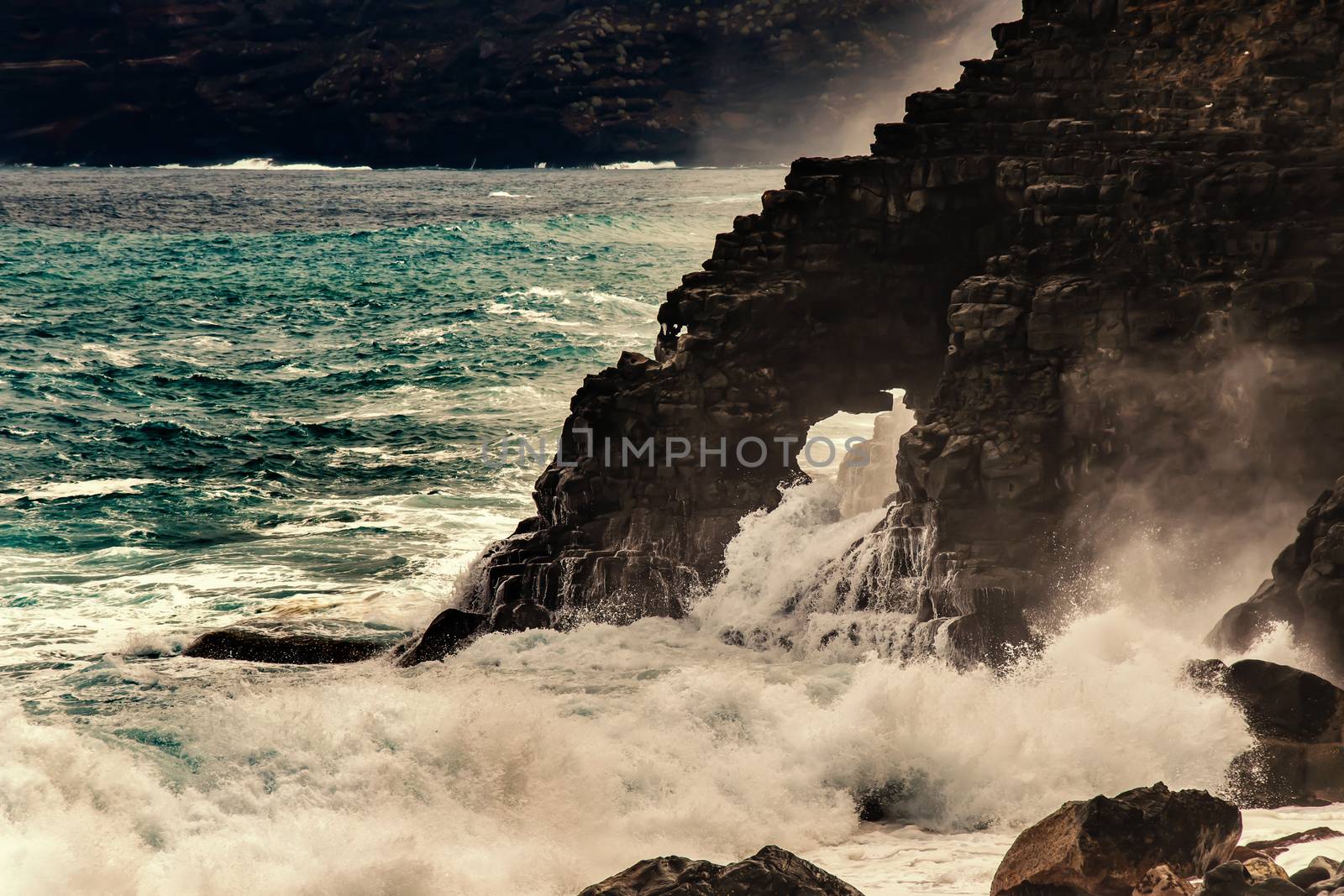 Ocean waves splash through, hole in rocks. Cave formation at shoreline in Tenerife. Aqua foam power scene. Stormy wave splashing with danger energy. Shore cliffs postcard vacations photography.