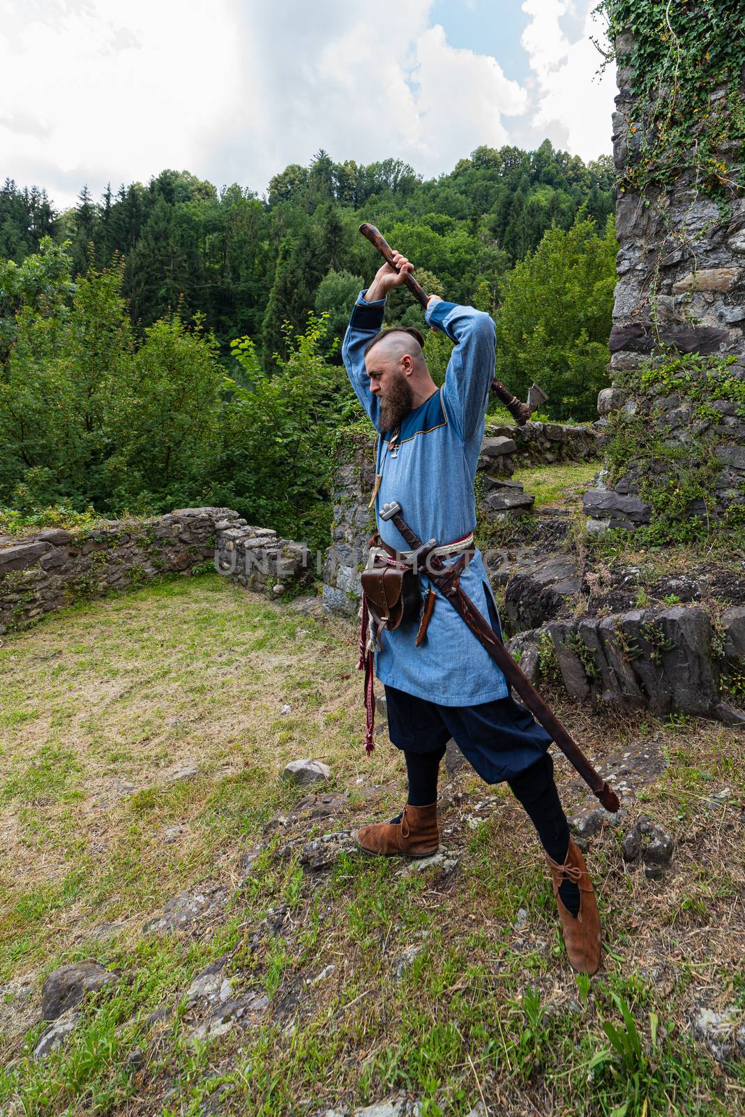 Viking warrior with thick beard brandishes an ax, an image of historical re-enactment among the medieval ruins