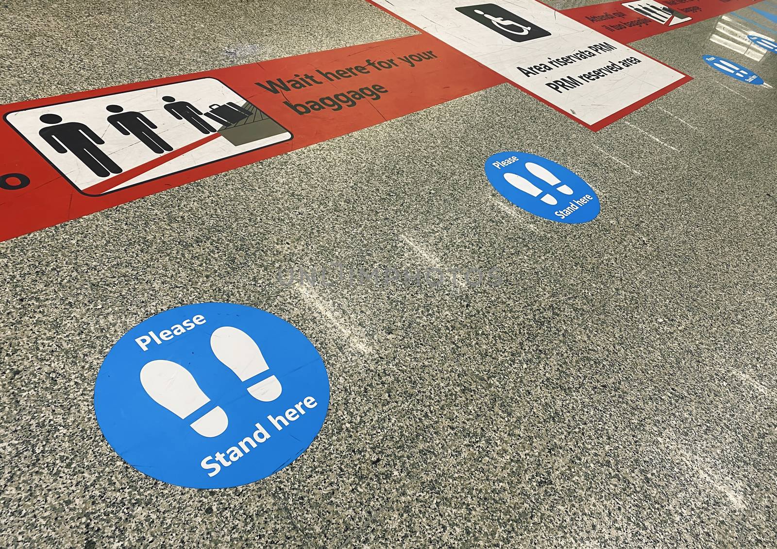 Stickers on the floor near the baggage claim belt at the airport that warn of keeping social distance during the health emergency during the coronavirus pandemic by rarrarorro