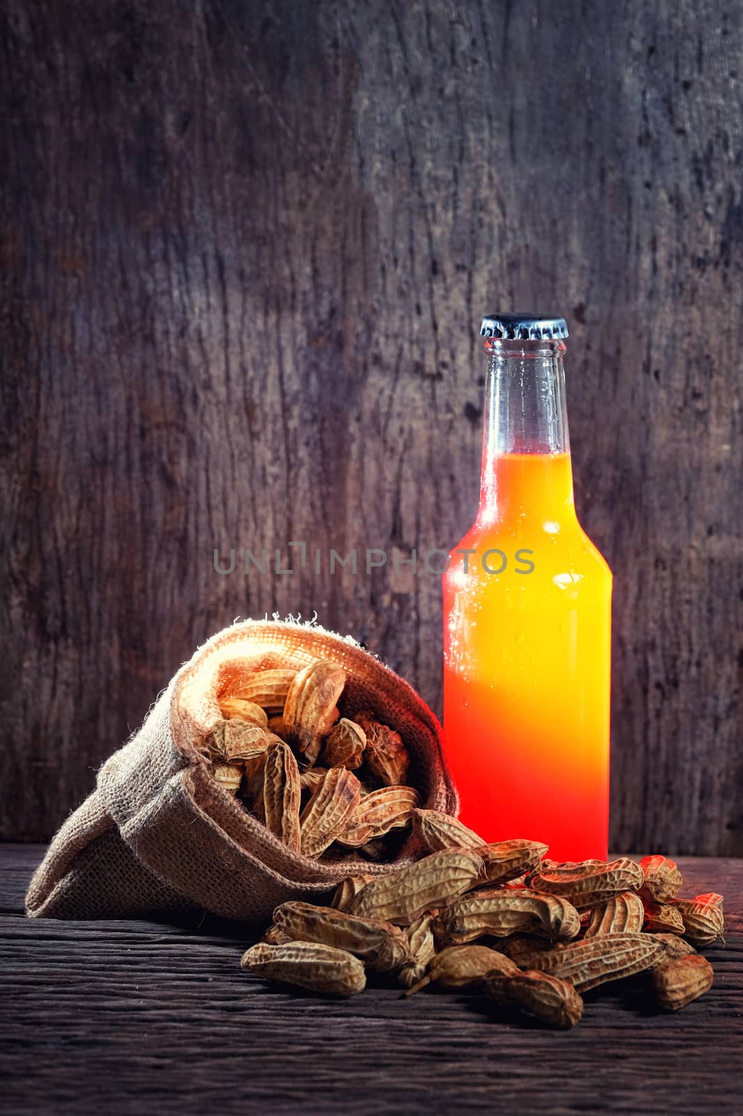 Peanuts and a Beer in red bottle in wood background by Surasak