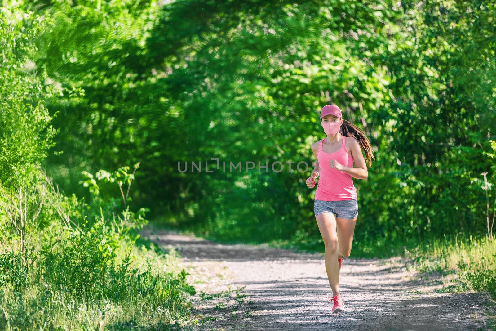 Mask corona virus COVID-19 running runner athlete wearing mask jogging outside on run workout in summer park nature. Sport lifestyle asian young woman.