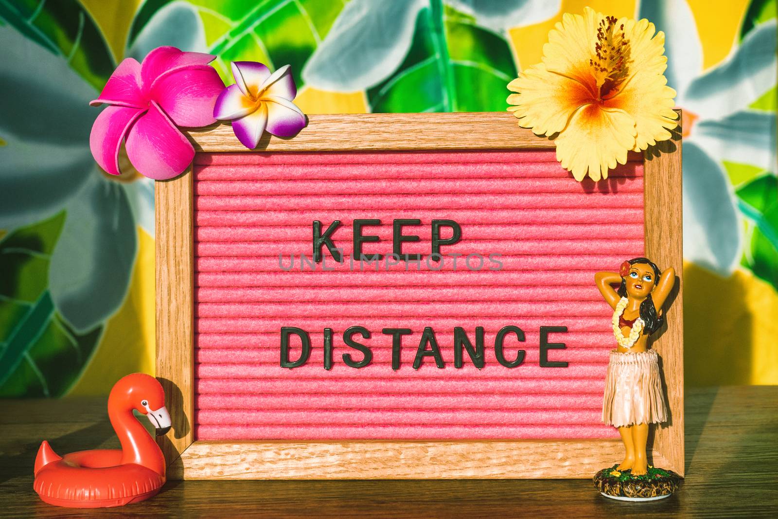 KEEP DISTANCE Covid-19 social distancing text sign for outdoor lifestyle people during summer. CORONAVIRUS concept. Tropical flowers felt board with hula dancer doll and pool float by Maridav