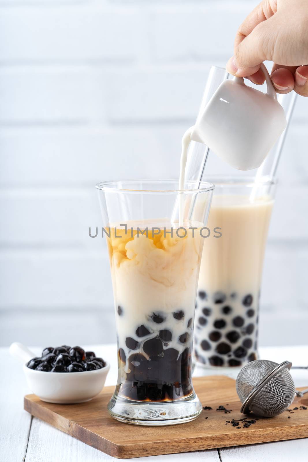 Making bubble tea, pouring blend milk tea into brown sugar pattern drinking glass cup on white wooden table background, close up, copy space