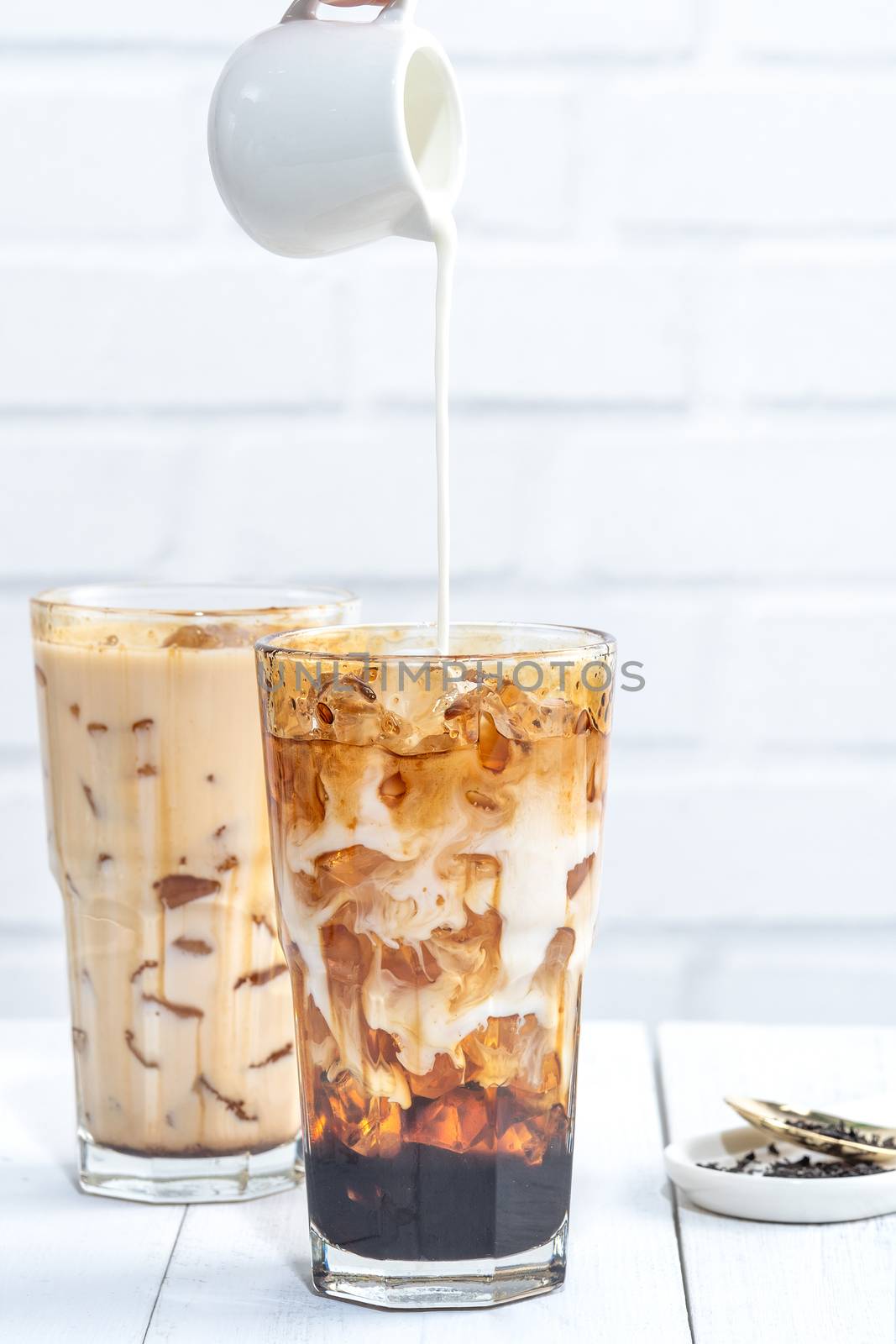 Making bubble tea, pouring blend milk tea into brown sugar pattern drinking glass cup on white wooden table background, close up, copy space