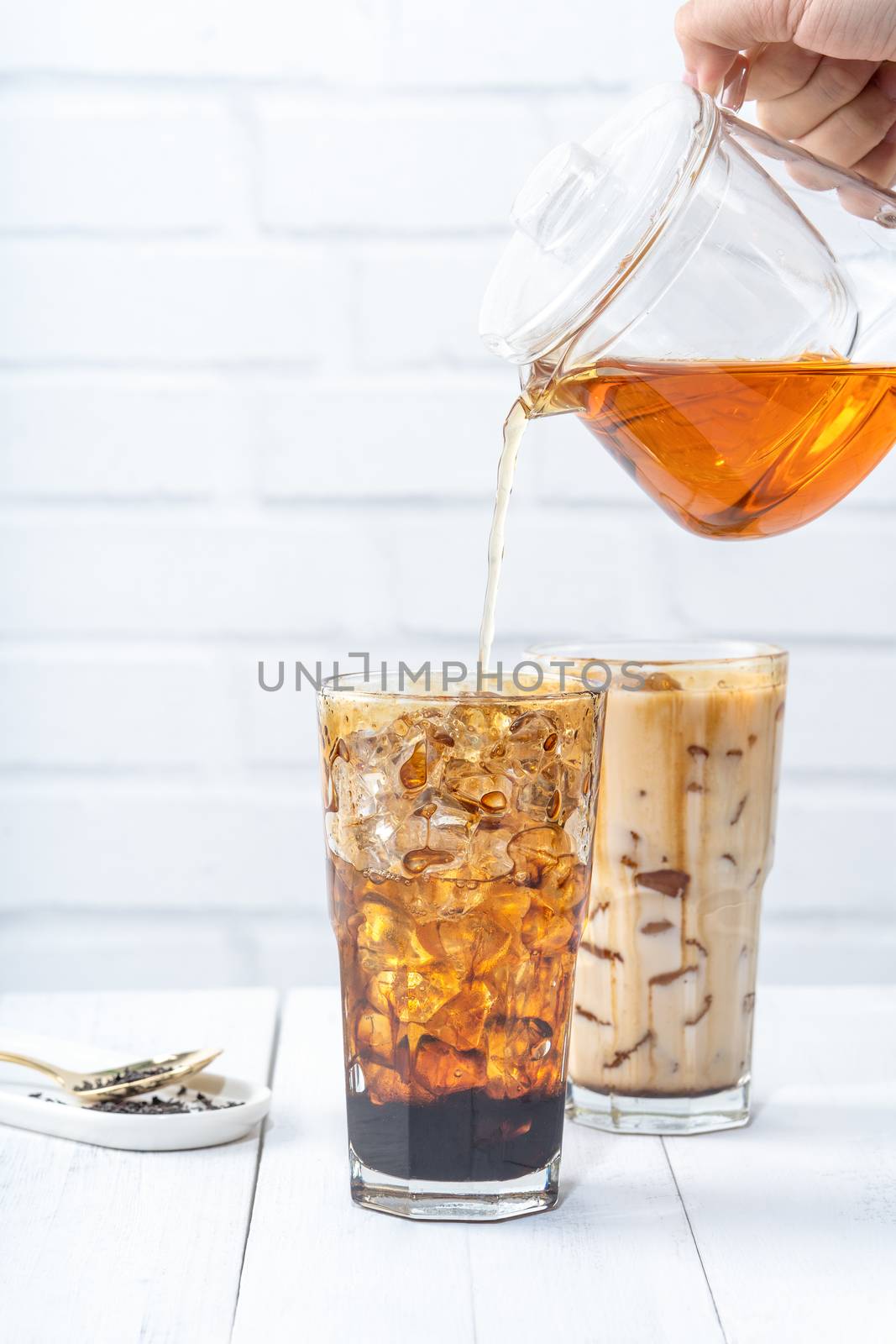 Making bubble tea, pouring blend milk tea into brown sugar pattern drinking glass cup on white wooden table background, close up, copy space
