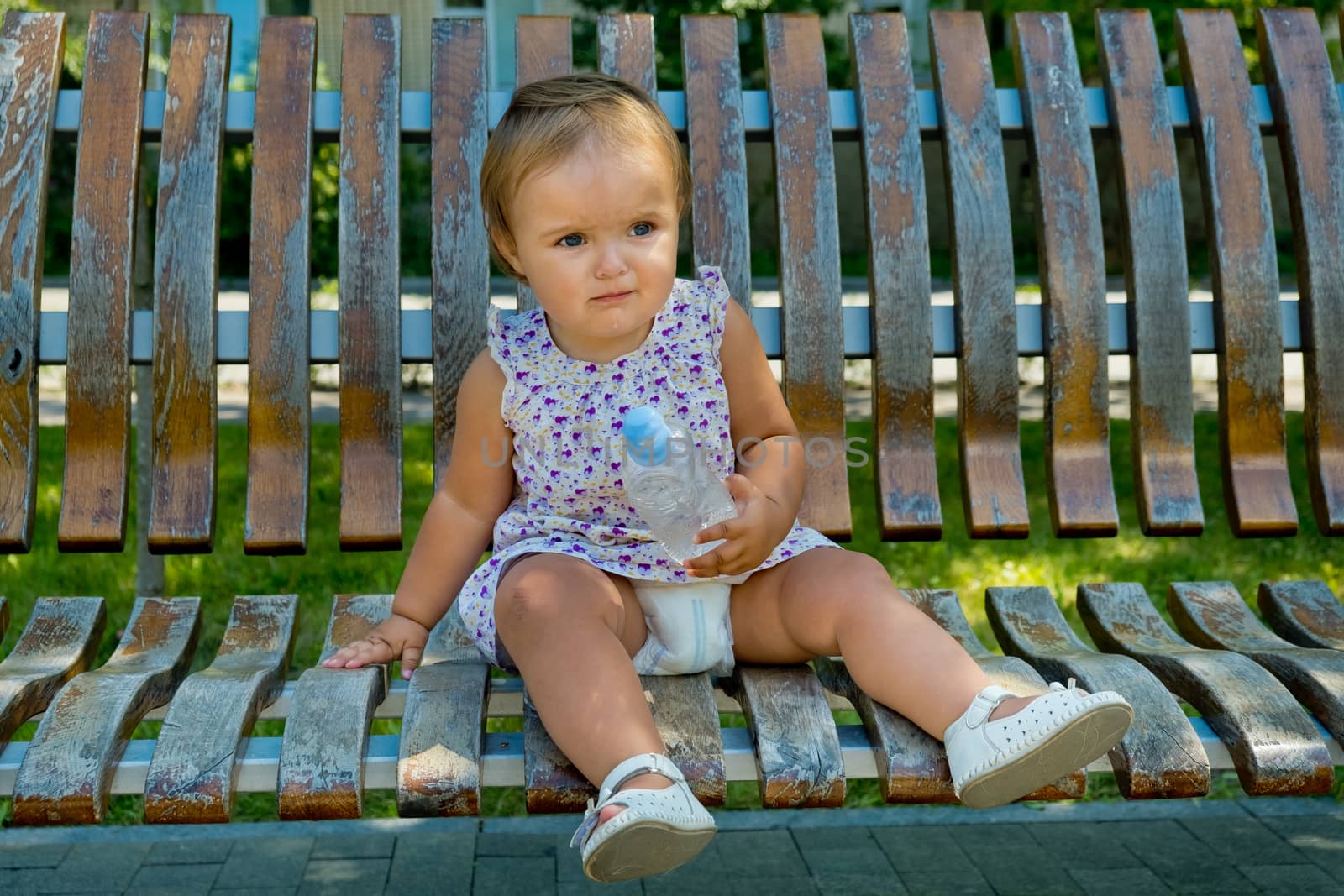 Little girl sits on a park bench with a bottle of water in her hands.