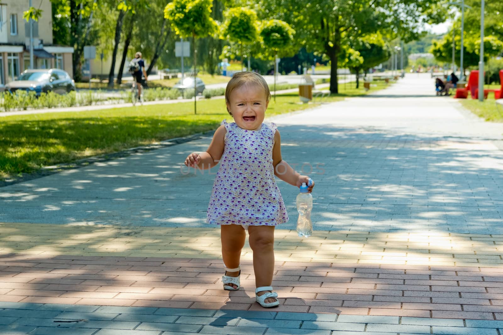 A little girl walks along the sidewalk and cries.