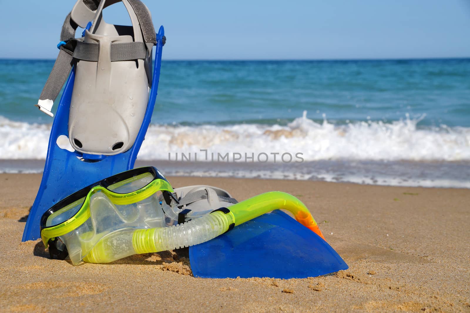 flippers and mask for swimming on the sand against the background of the sea and clear sky, copy space