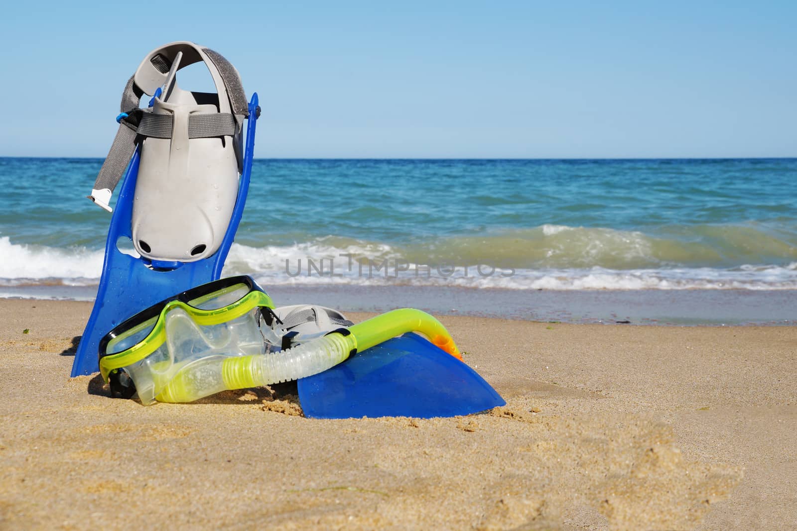 flippers and mask for swimming on the sand against the background of the sea and clear sky, copy space